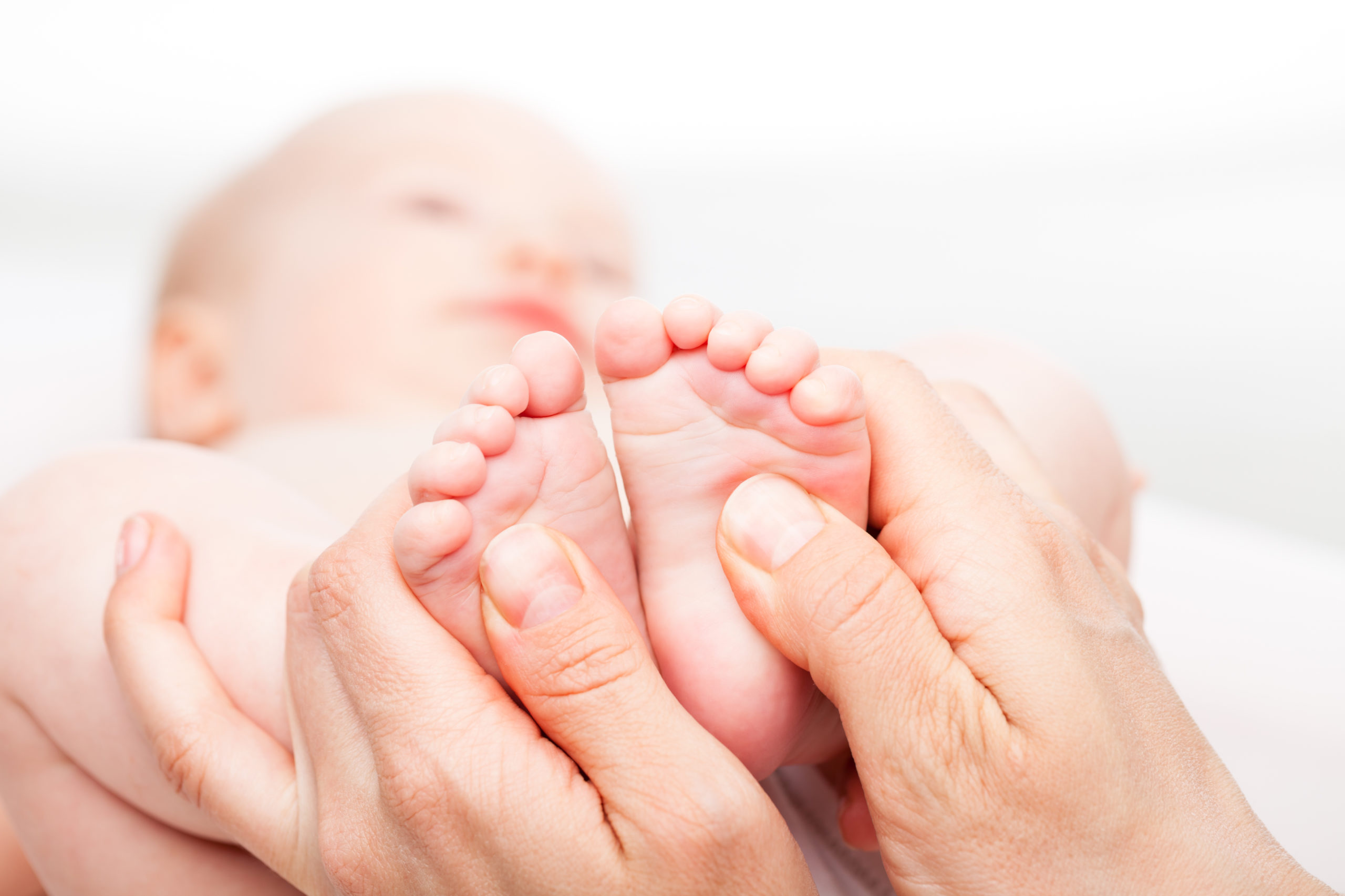 Close-up shot of three month baby girl receiving foot massage from a female massage therapist. Camera is focused on infant's feet. Face is blurred in background.